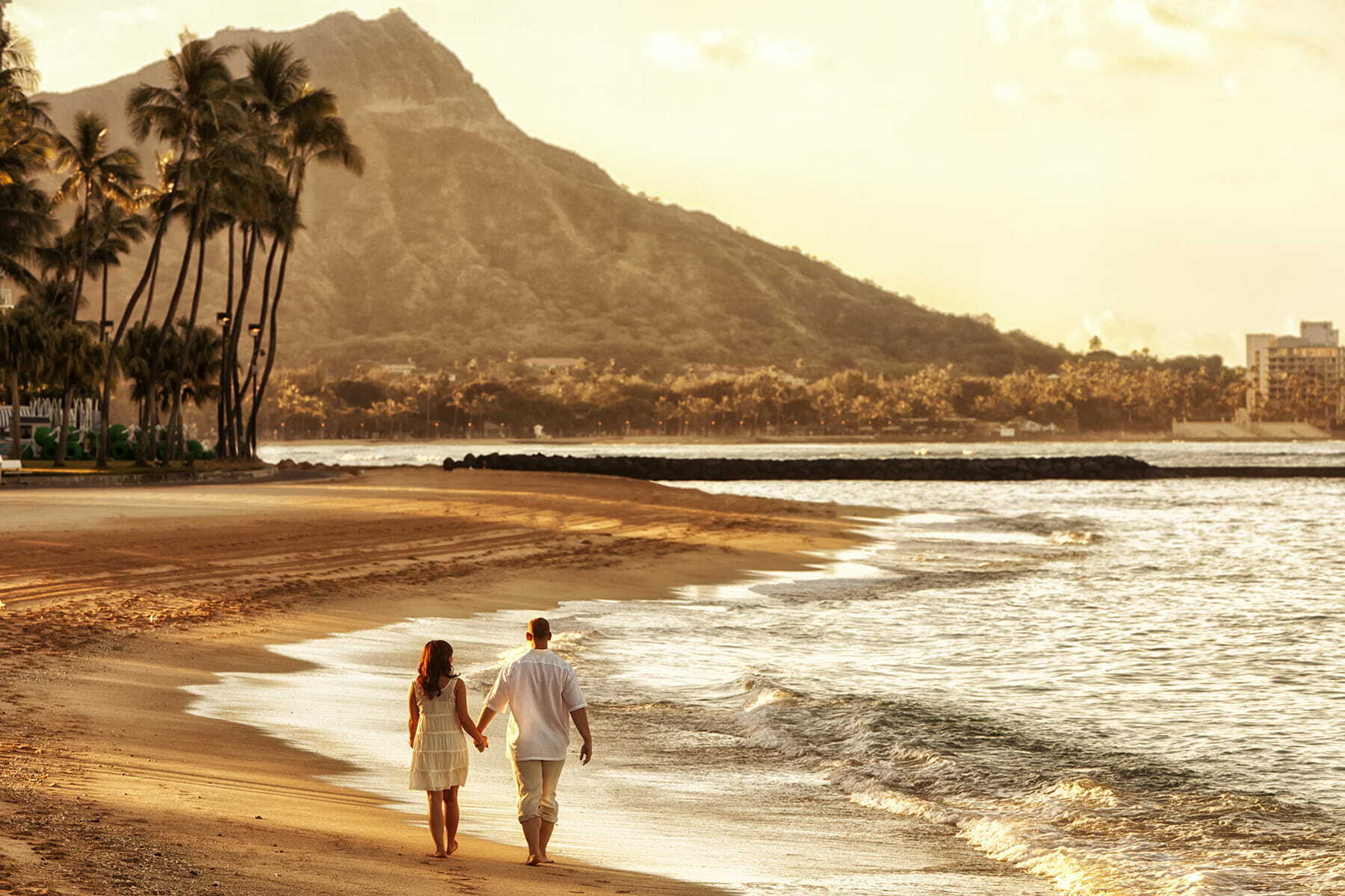 A couple walking along Waikiki Beach with a perfect view of Diamond Head.